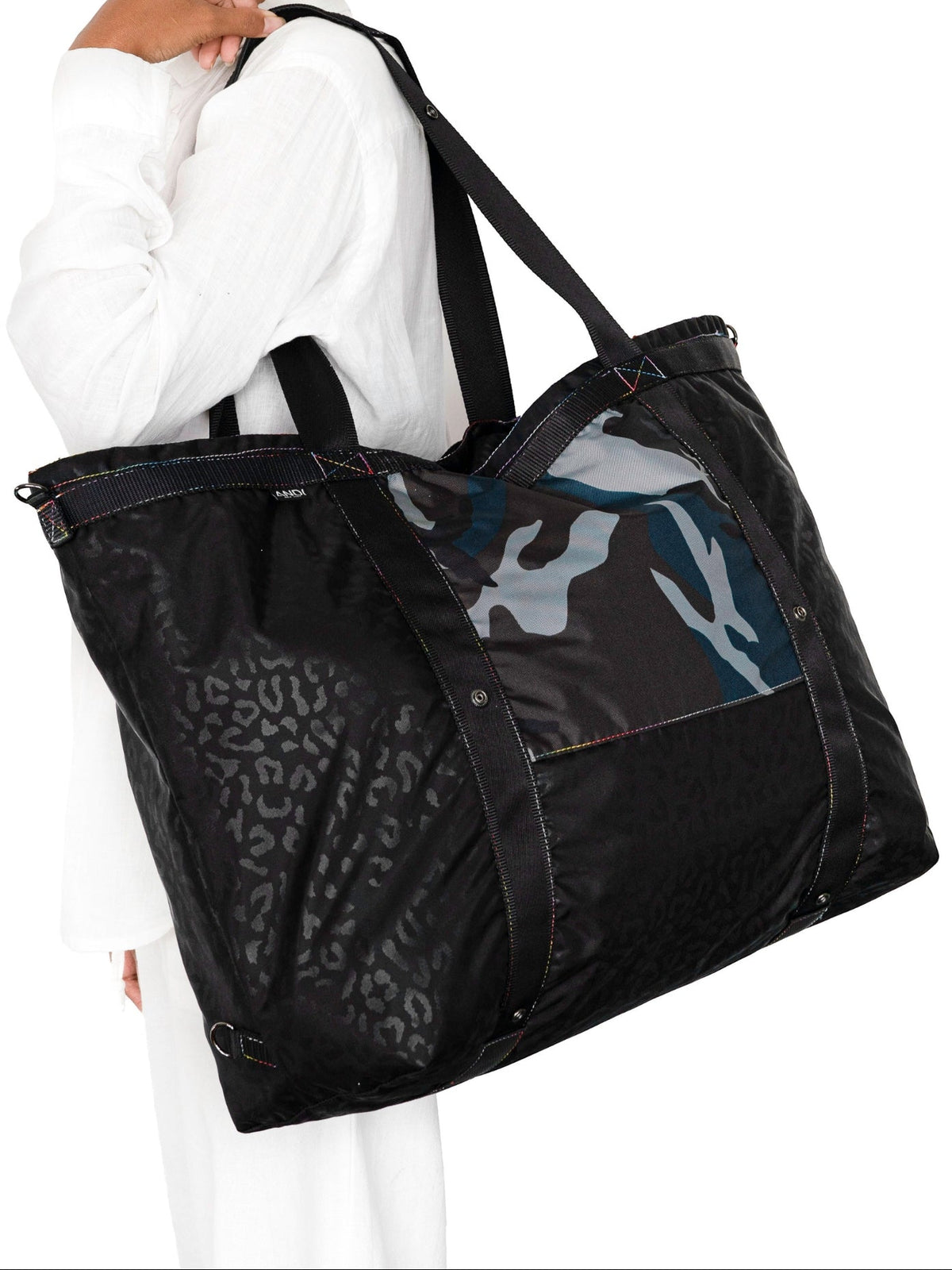 Black tote bag with camouflage and leopard print sections worn by a person on a white background