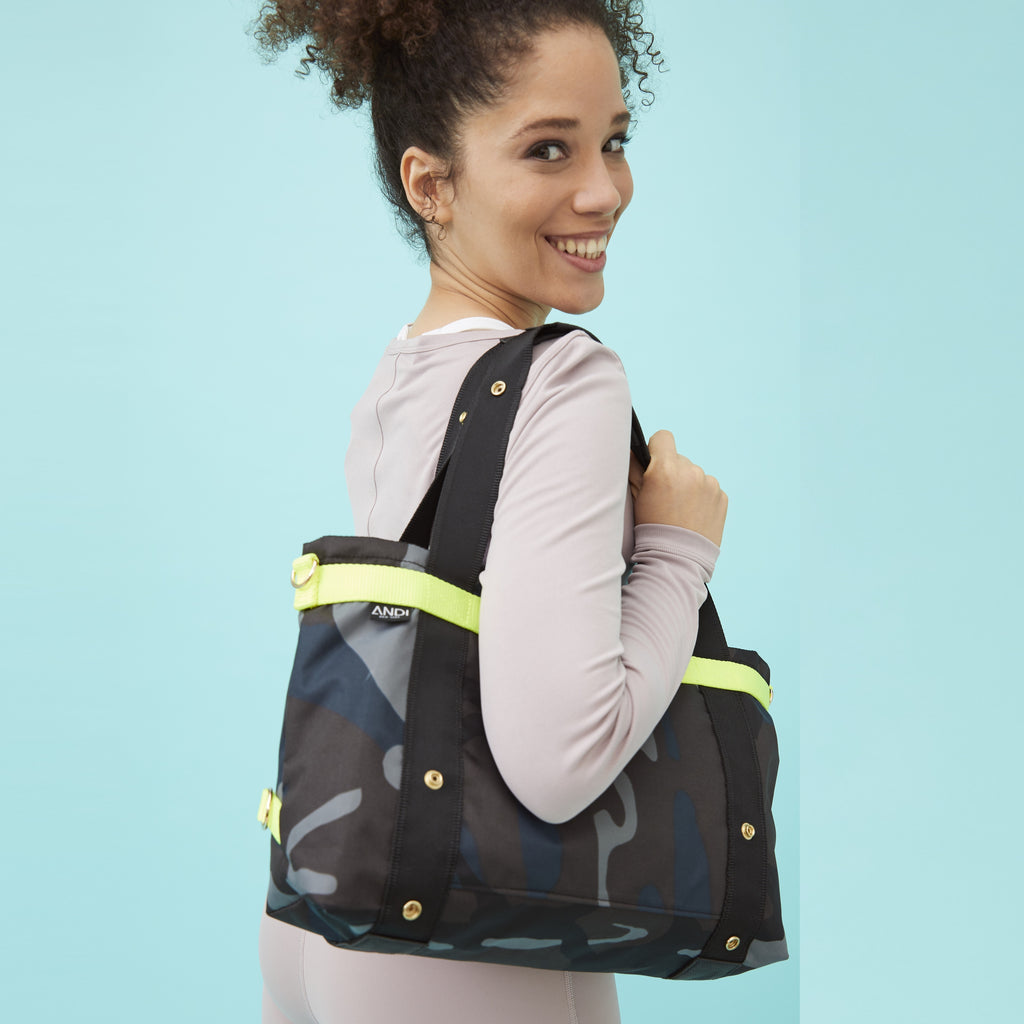 Model carrying convertible ANDI Small crossbody tote on her shoulder | Blue camo with hot yellow