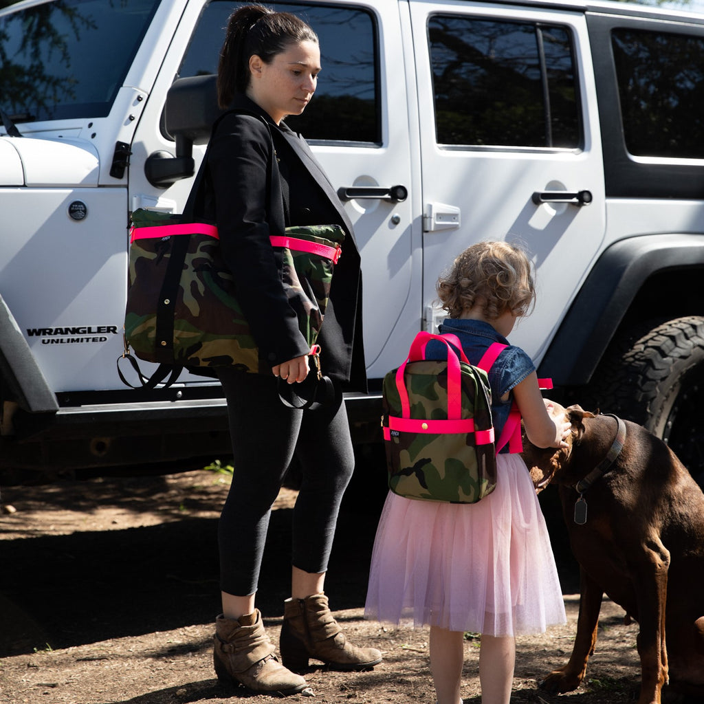 A girl and woman wearing matching ANDI bags in Camo with hot pink straps | Water resistant nylon