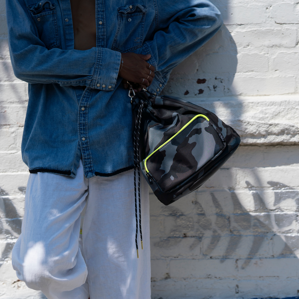 Woman holding stylish ANDI bucket bag in grey camo with neon yellow | water resistant nylon